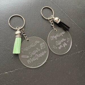 Porte-clés personnalisés en plexiglas pour maîtresse et ATSEM. Modèles gravés Pascaline Super Maîtresse avec pompon vert et Angélique Atsem en or avec pompon noir.