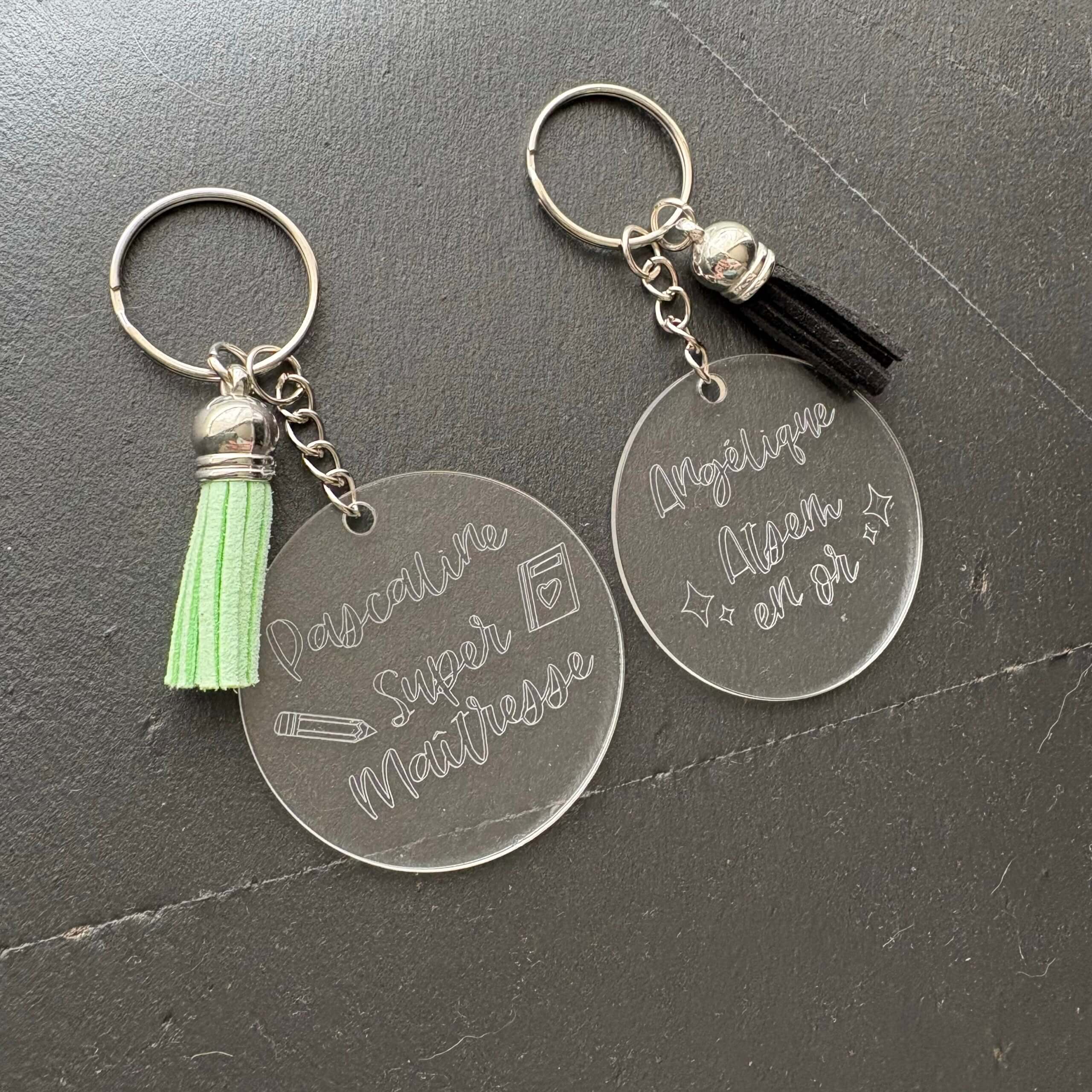 Porte-clés personnalisés en plexiglas pour maîtresse et ATSEM. Modèles gravés Pascaline Super Maîtresse avec pompon vert et Angélique Atsem en or avec pompon noir.
