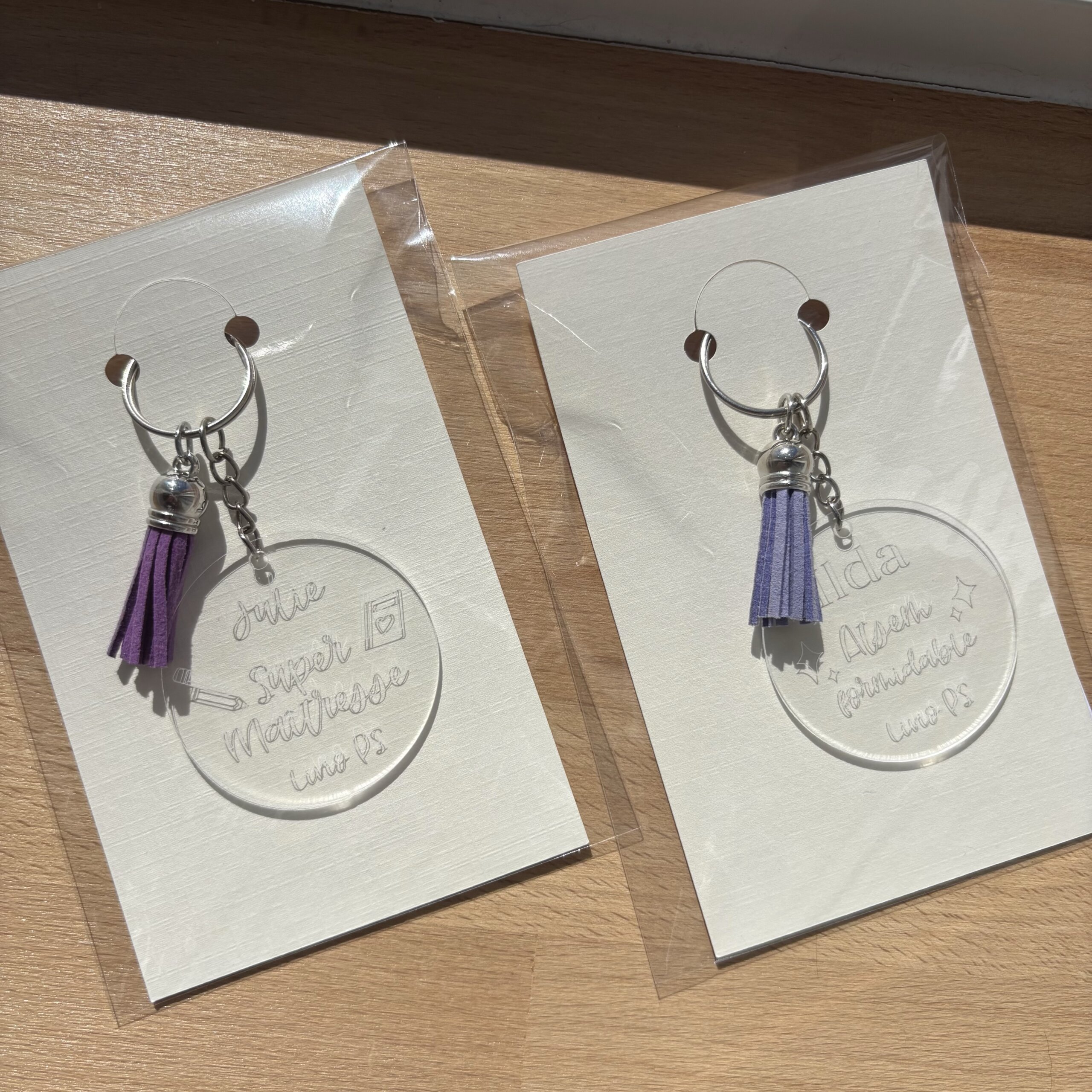 Deux porte-clés personnalisés en acrylique transparent pour maîtresse et ATSEM avec pompons violets
