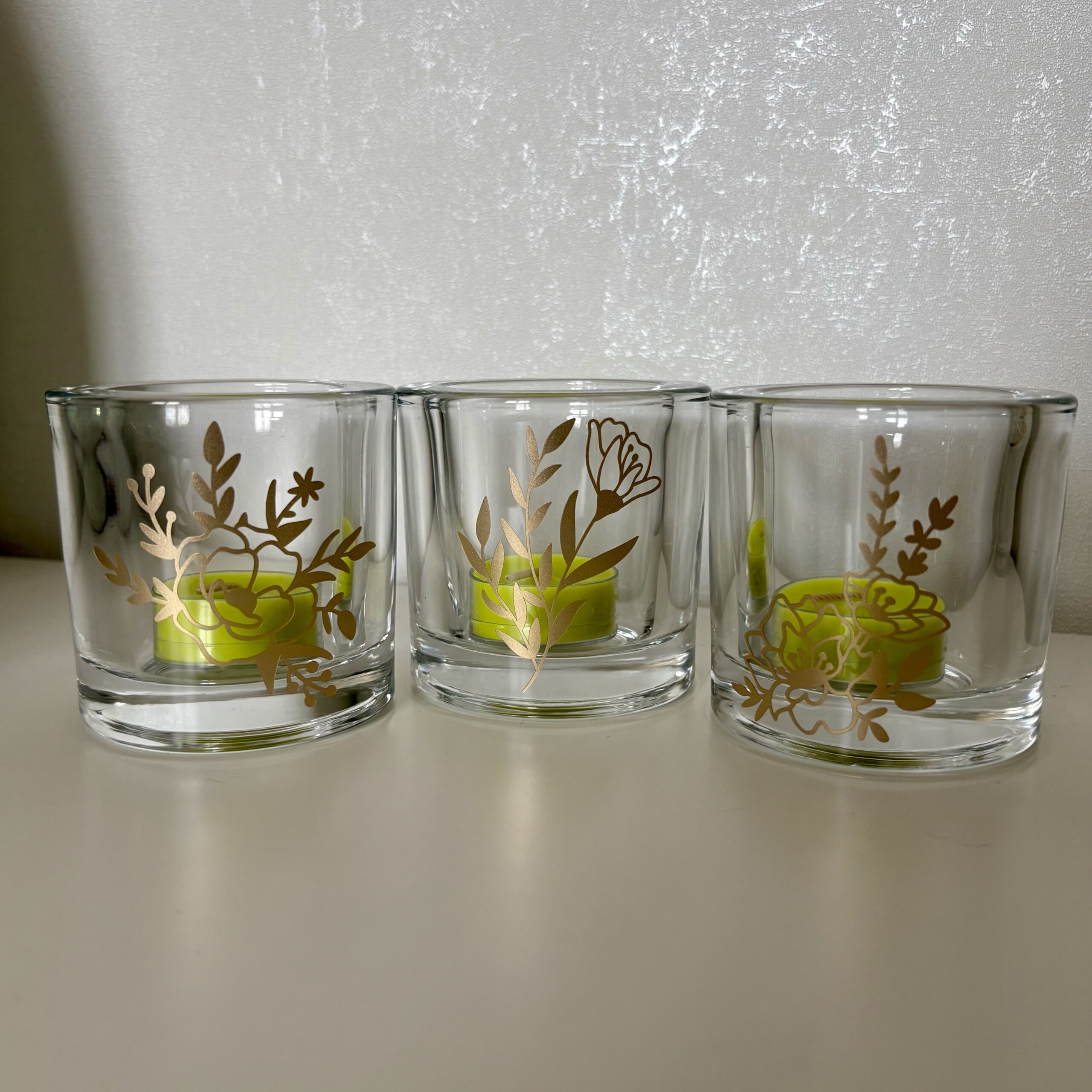 Trois photophores en verre transparent avec motifs floraux dorés Trois photophores en verre transparent avec motifs floraux dorés et bougies chauffe-plat vertes à l'intérieur