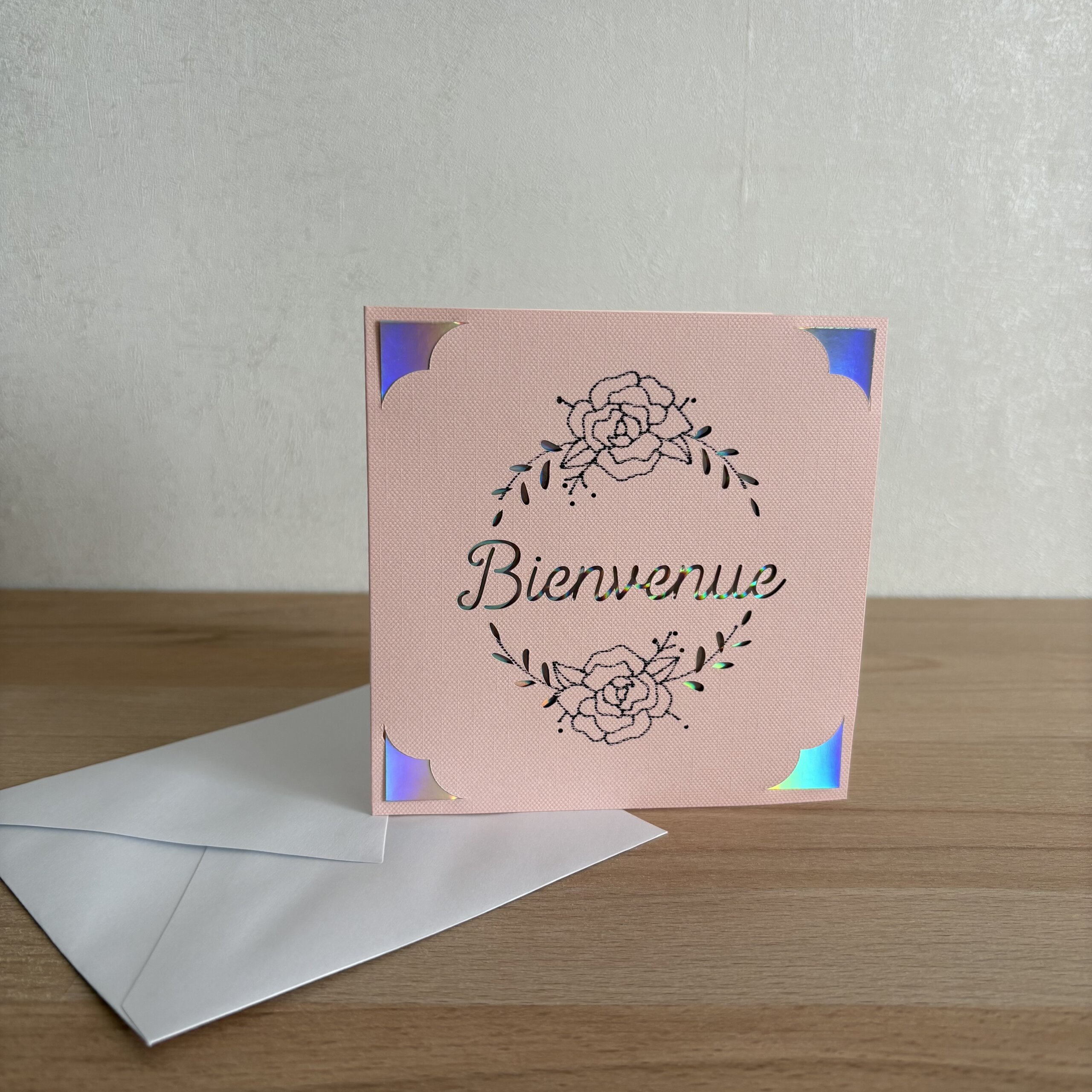 Carte Bienvenue rose faite main en papier texturé avec fleurs et détails holographiques, idéale pour une naissance