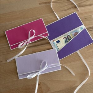 Trois pochettes à billets faites main en papier texturé rose, lilas et violet, dont une ouverte avec un billet