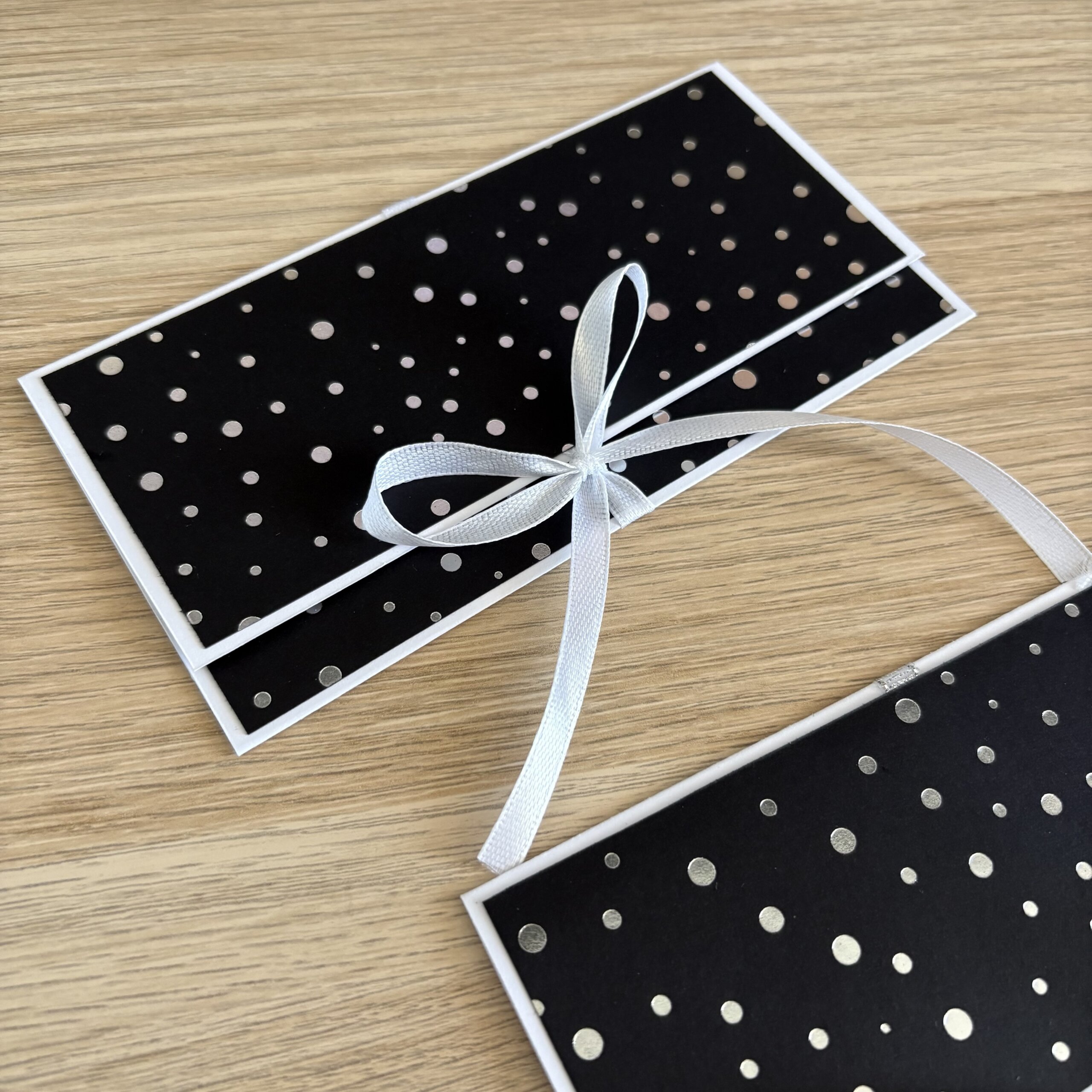 Pochette cadeau pour billets noire à pois argentés fermée par un ruban blanc