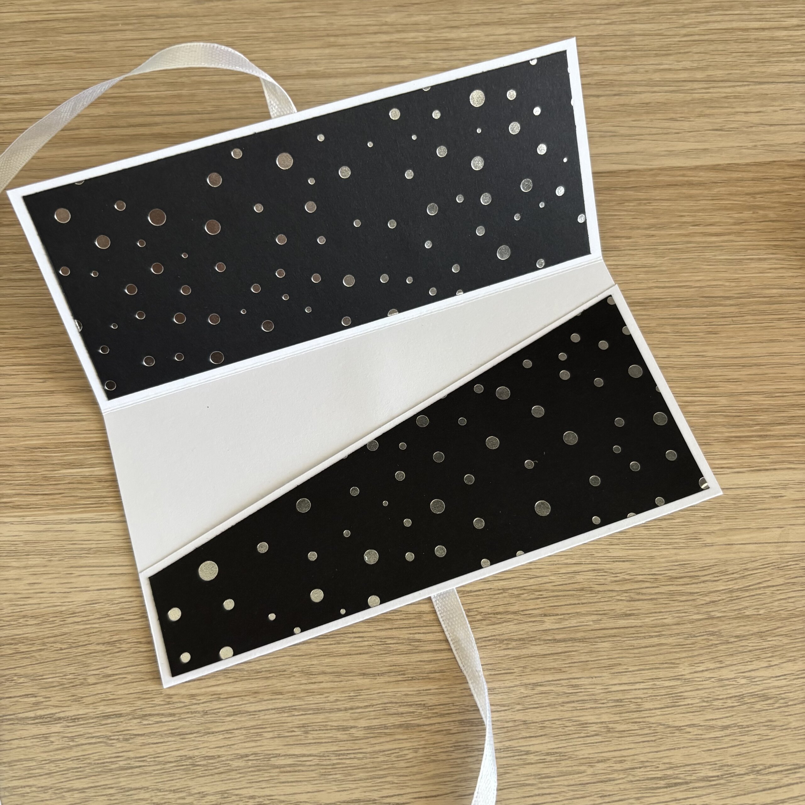 Intérieur d’une pochette cadeau noire à pois argentés avec emplacement prévu pour glisser les billets