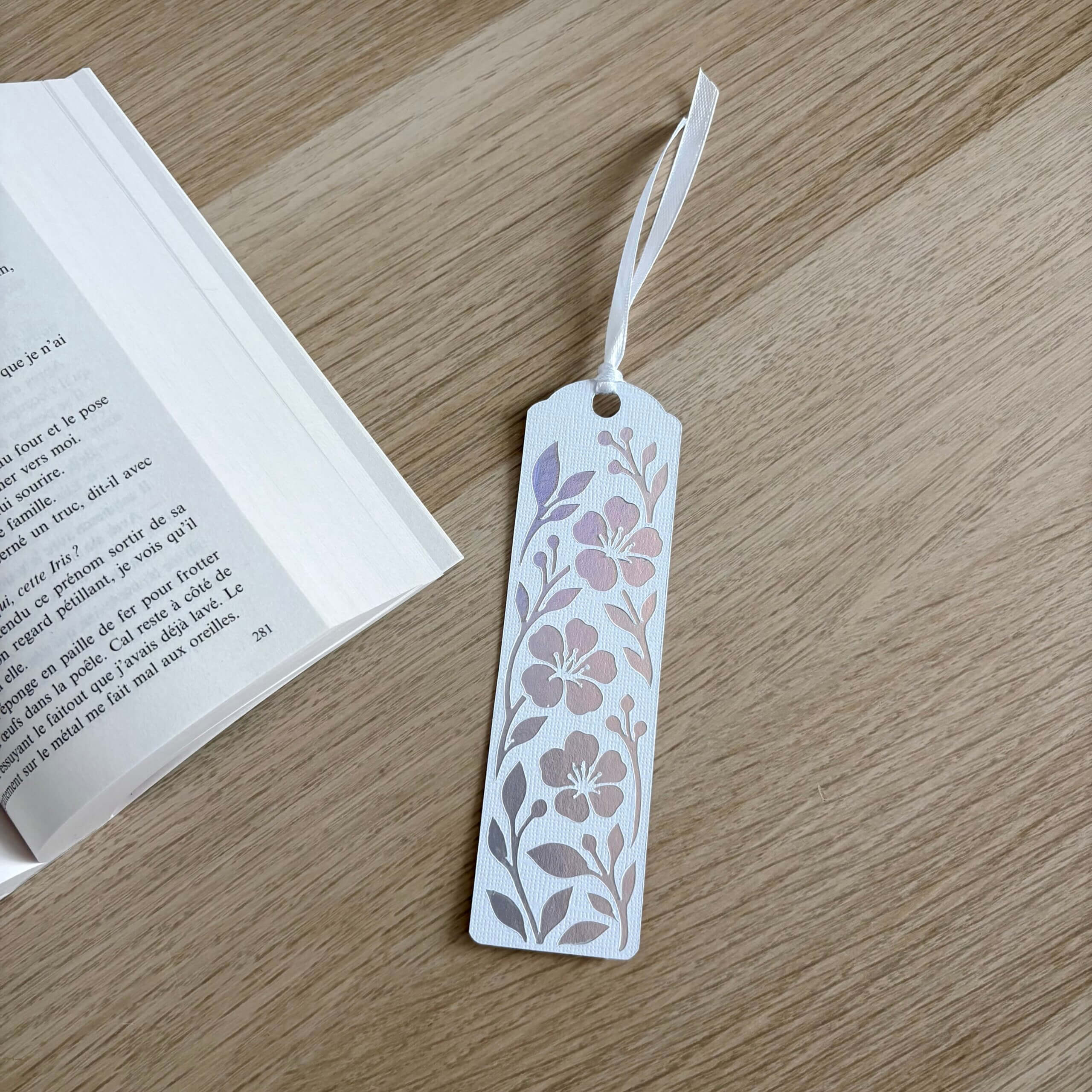 Marque-page fleuri en papier blanc texturé avec motifs fleurs et feuillage en papier miroir holographique et ruban blanc