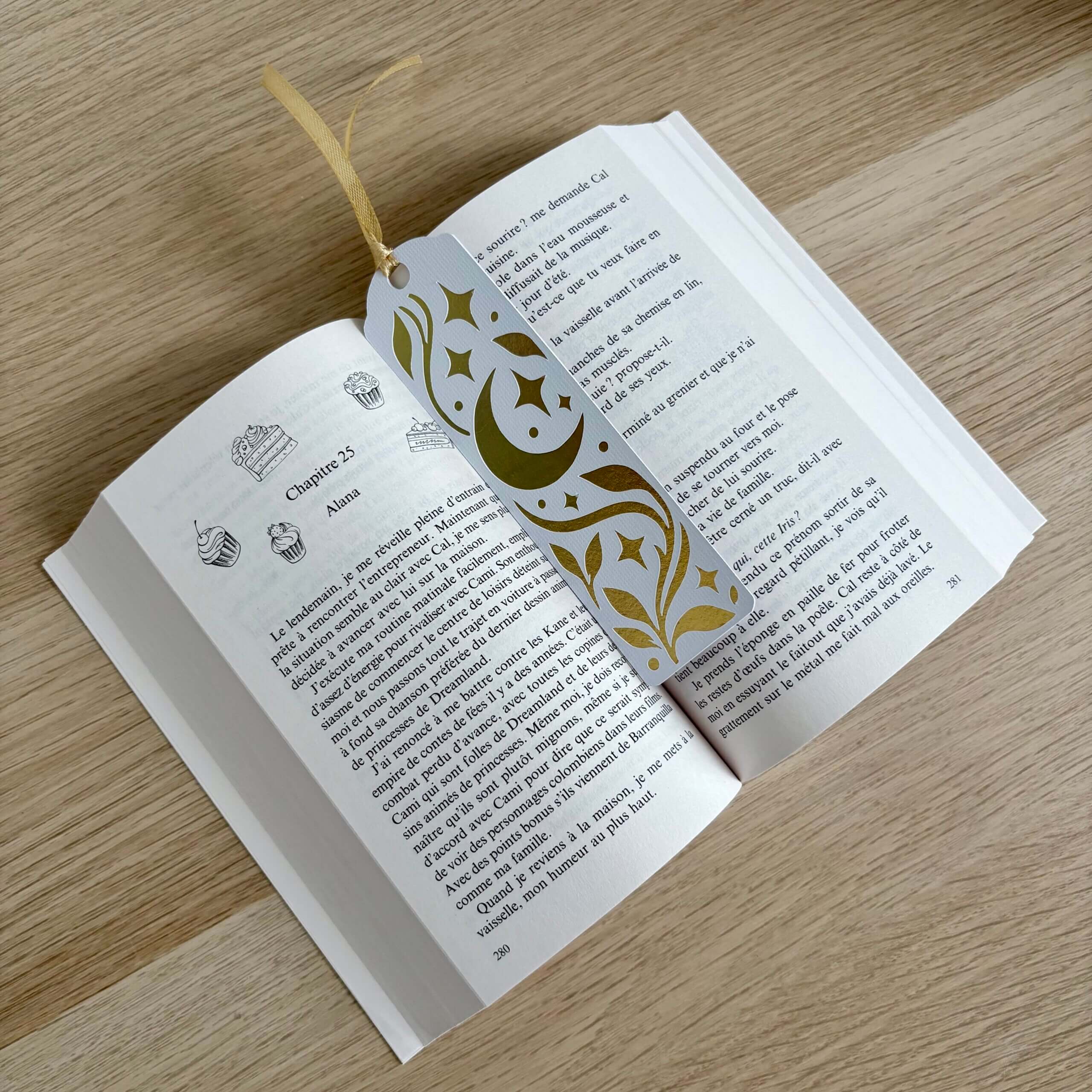 Marque-page lune et étoiles en papier blanc texturé et papier miroir doré, présenté dans un livre ouvert